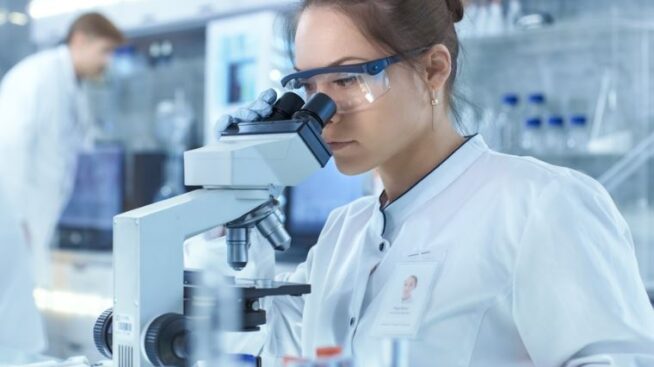 Female researcher in lab peering through microscope