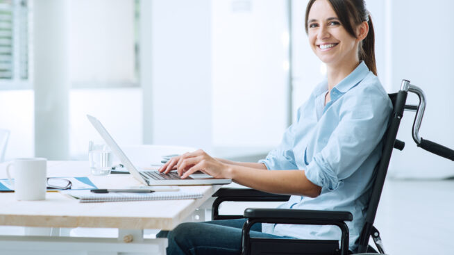 Smiling woman in wheelchair at desk viewing webinar series