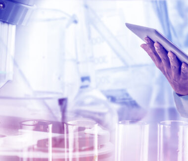 Modern lab with microscope and lab technicians hand holding a computer tablet as they type